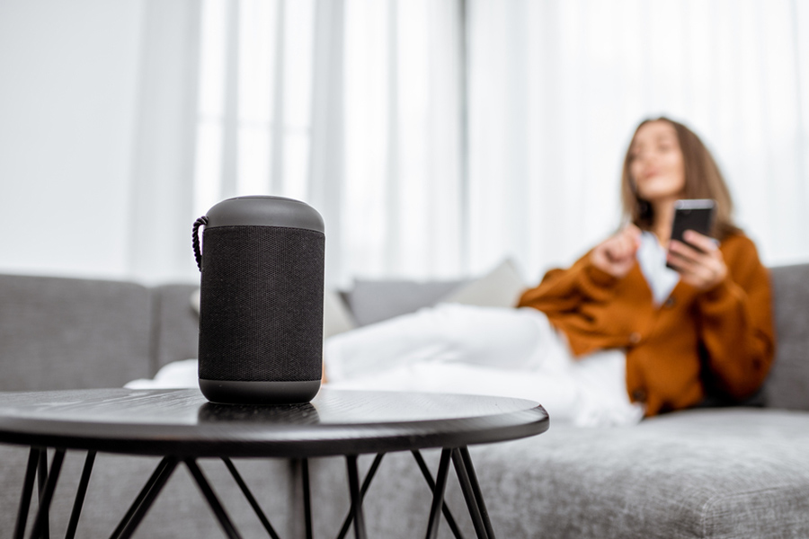 Use a smart speaker to conveniently control other devices in your Bloomington apartment. Woman sitting on a sofa beside a smart speaker on a coffee table